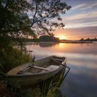 Tranquil lake scene: Twilight, lone boat, two individuals, overhanging branches