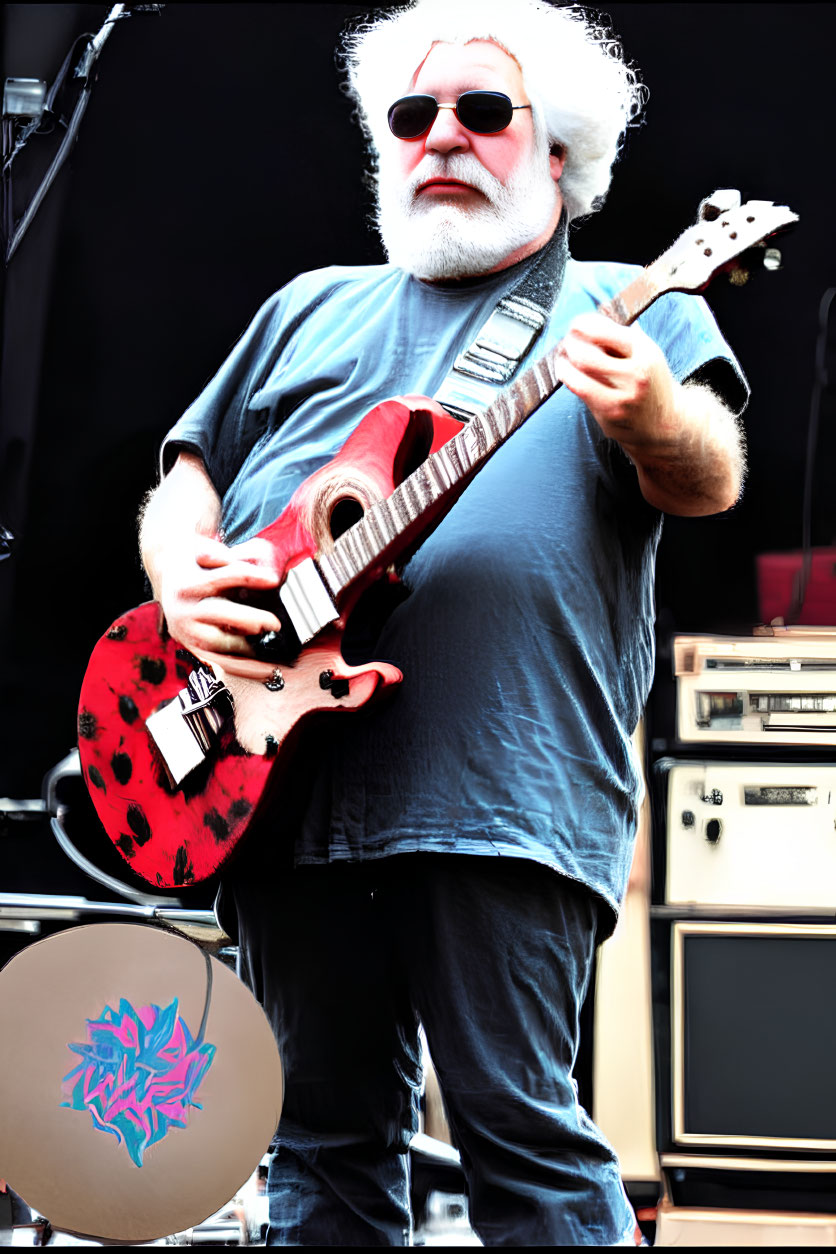 White-haired musician plays red electric guitar on stage with sunglasses and beard.