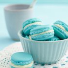 Blue Macarons Stack with Bowl, Spoon, and Candies on Soft Blue Background