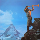 Person playing trumpet on rocky peak with distant mountain view