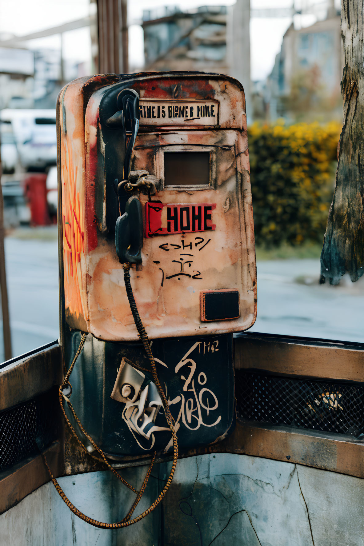 Vandalized payphone with graffiti and dangling handset in public booth