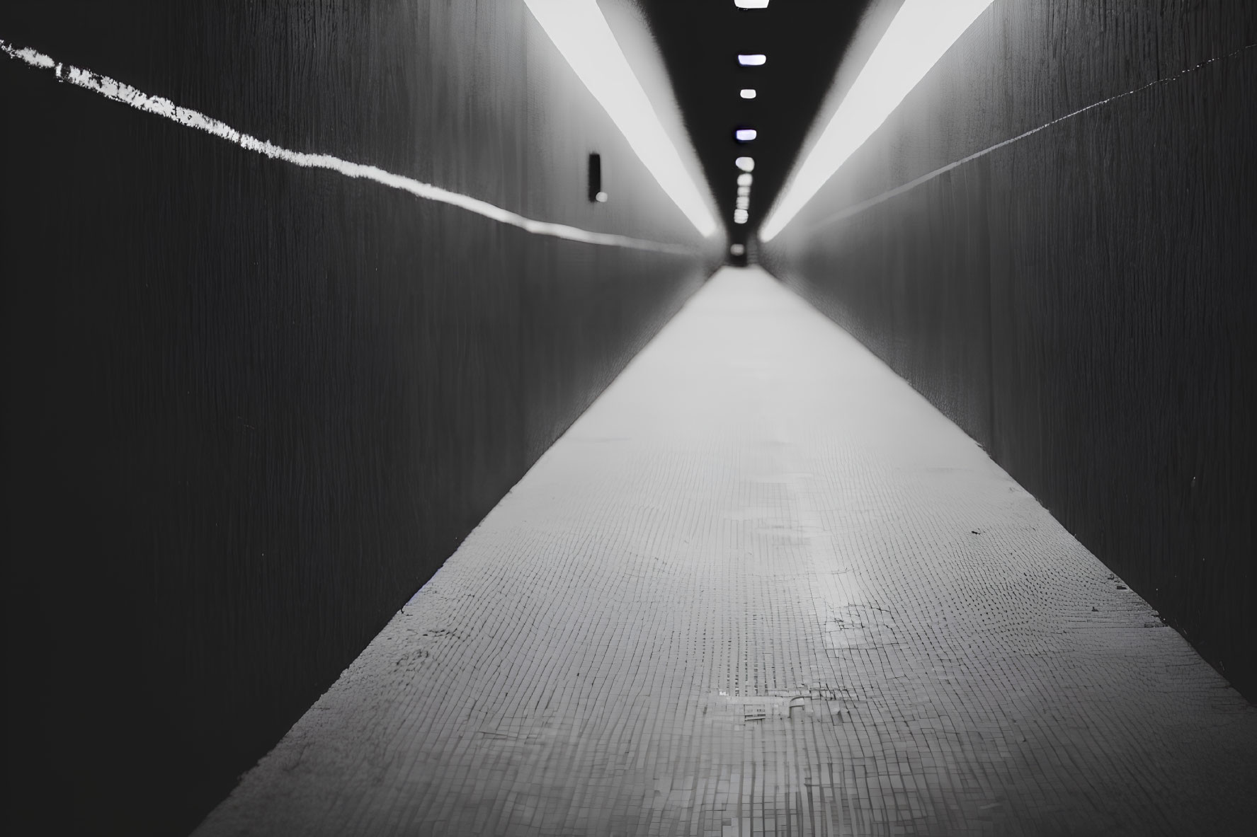 Monochrome photo of long, narrow corridor with bright overhead light strip and reflective floor
