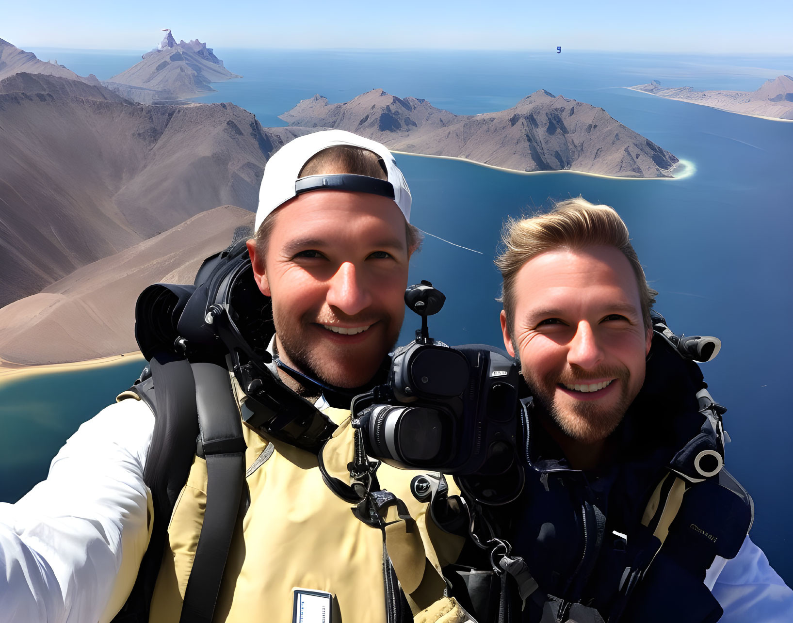 Men taking selfie with mountainous coastline backdrop.