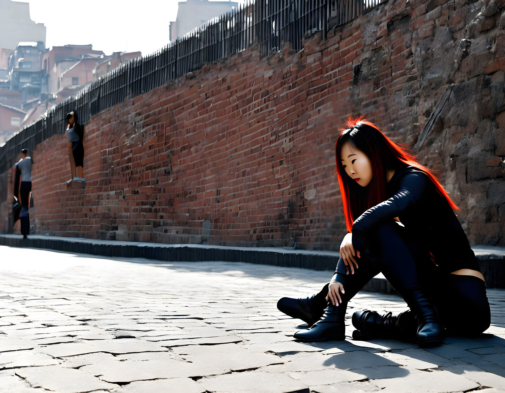 Red-haired person crouching on cobblestone path by brick wall in sunlight