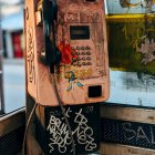 Vandalized payphone with graffiti and dangling handset in public booth