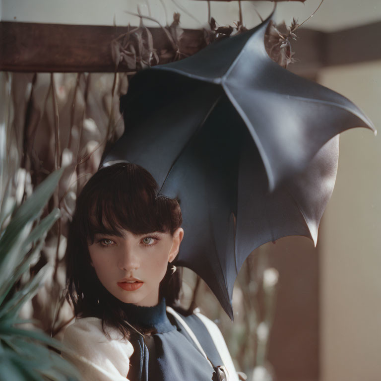 Dark-haired woman with blue eyes holding bat wing-like umbrella in botanical setting