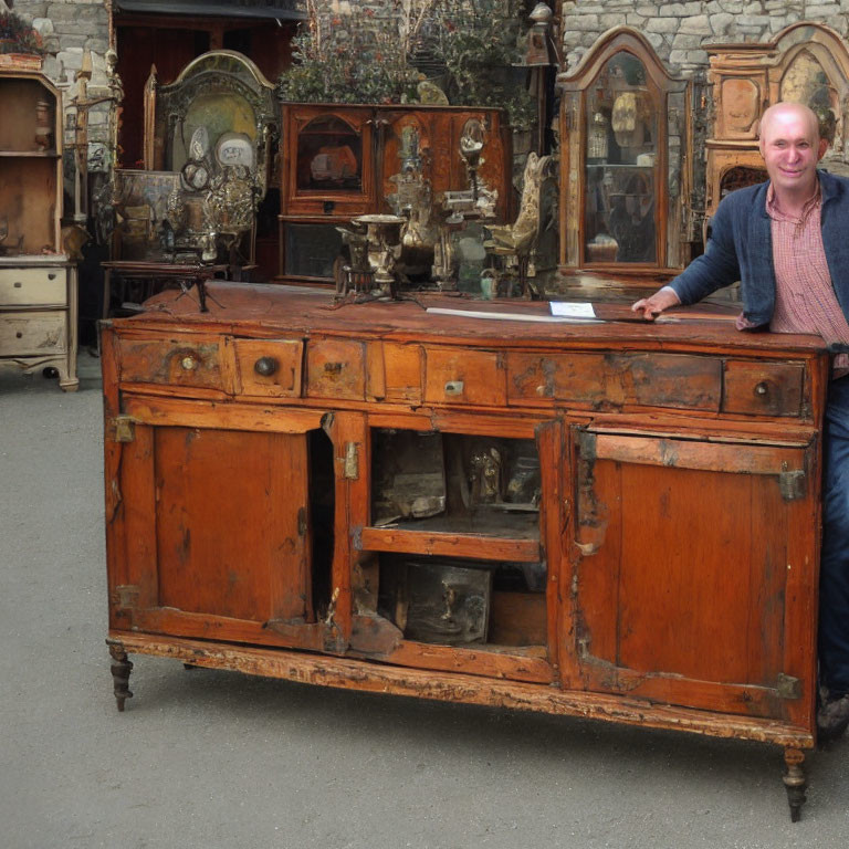 Man standing by antique wooden sideboard with vintage items in background