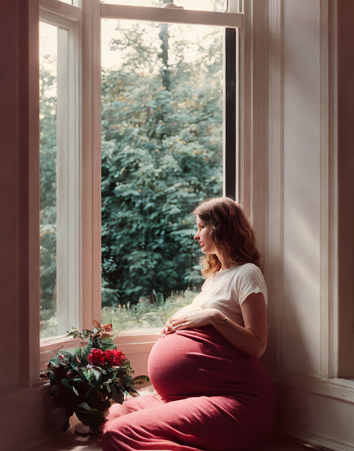 Pregnant person sitting by window with natural light and potted plant