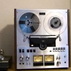 Person smiling next to stylized reel-to-reel tape recorder with face-like design