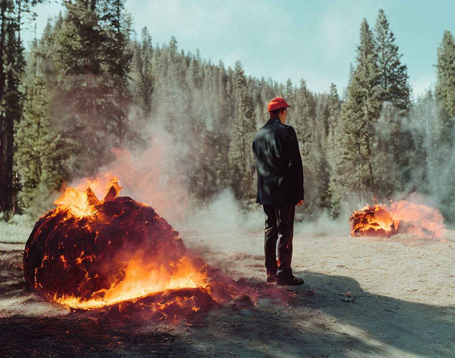 Person in Black Suit and Red Hat Observing Smoldering Tree Logs in Forest Clearing