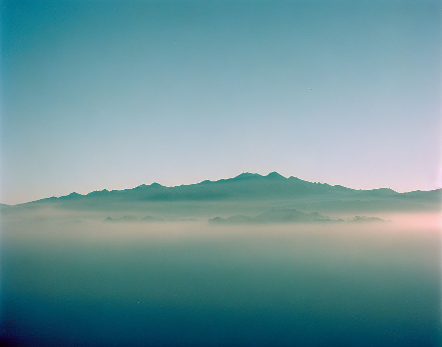 Tranquil blue landscape with misty mountains and clear sky.