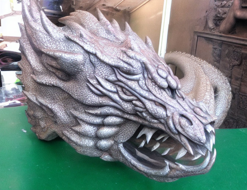 Detailed Dragon Head Sculpture with Textured Scales and Sharp Teeth on Green Surface