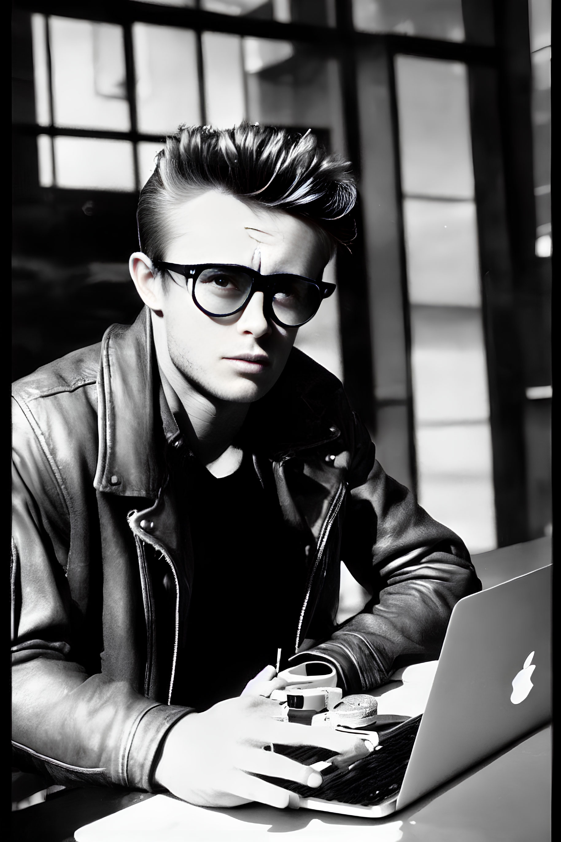 Young man with pompadour hairstyle and glasses works on laptop outdoors