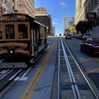Scenic view of cable car on San Francisco street with parked cars and buildings under blue sky