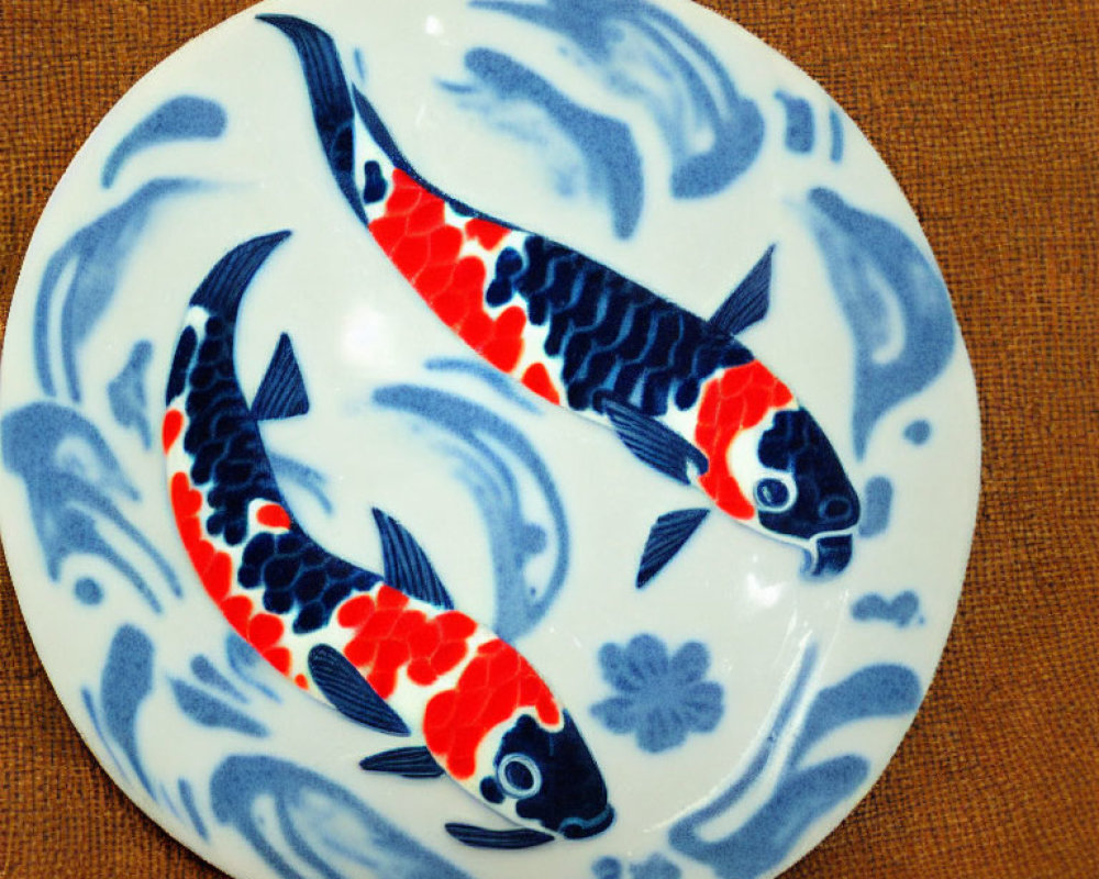 Circular ceramic plate with orange and black koi fish on blue and white wave design
