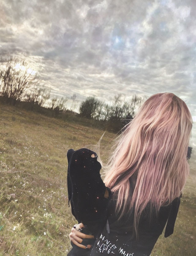 Pink-haired person with backpack in field gazes at cloudy sky