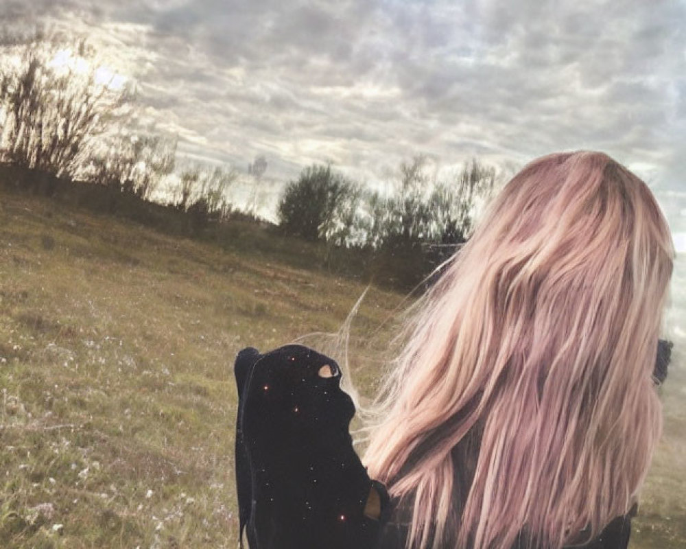 Pink-haired person with backpack in field gazes at cloudy sky
