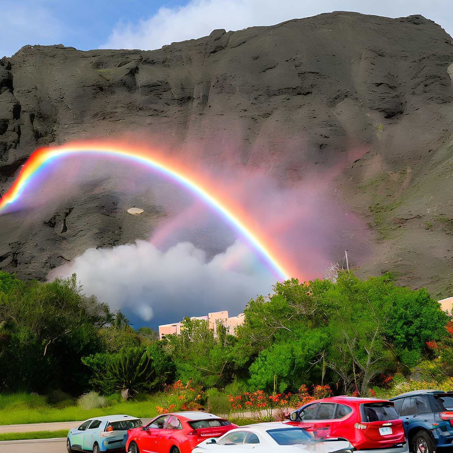 Colorful rainbow over parking lot with cars and hillside landscape