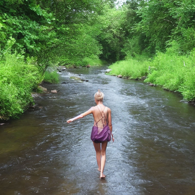 Hiker in backpack wading in stream amid lush greenery