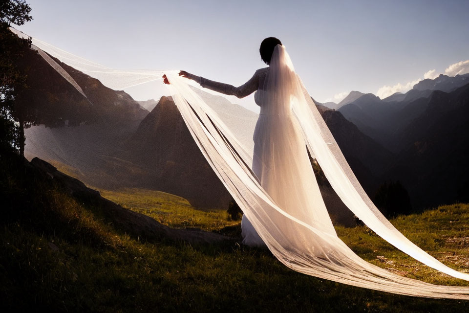 Woman in white dress with flowing veil against mountain backdrop at sunset