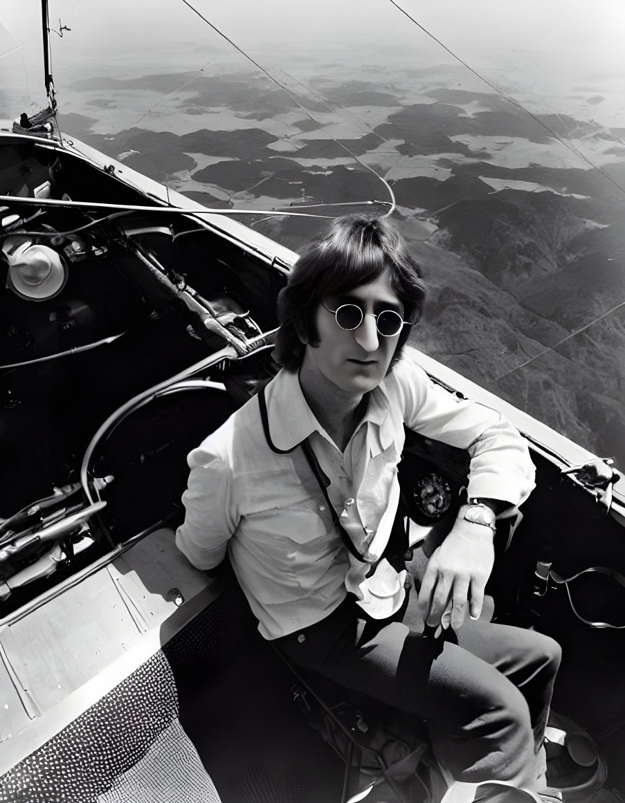 Person in round sunglasses sits confidently in aircraft cockpit with panoramic mountain view.