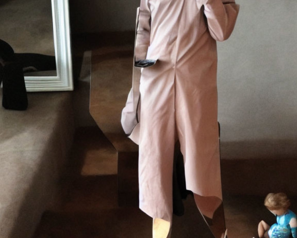Person in pink oversized outfit mimics mirror reflection next to doll