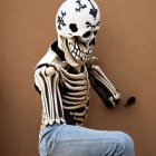 Person in Skull Mask and Skeleton Costume Posing on Brown Background