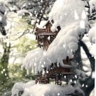 Snow-covered treehouse with warmly lit windows in winter landscape