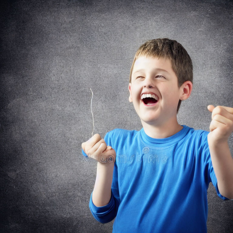 Young boy in blue shirt laughing with textured gray background.