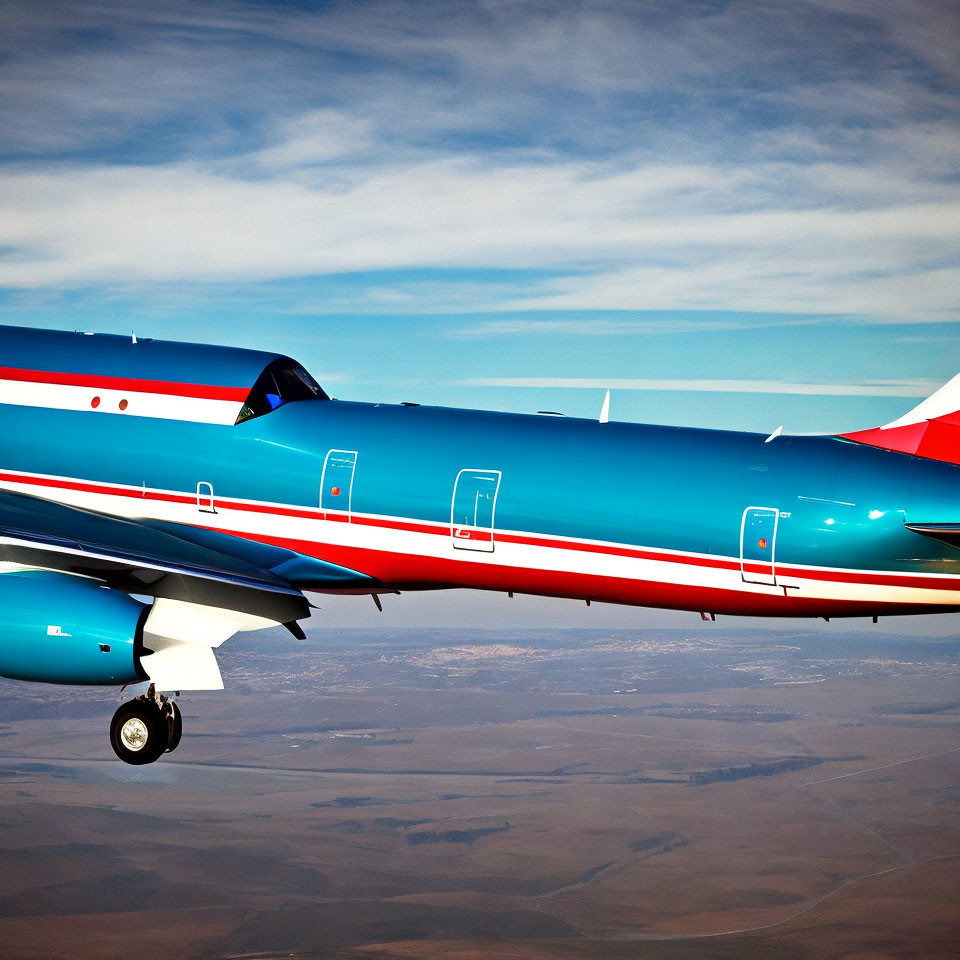 Vibrant blue and red jet soaring in blue skies over distant brown landscape