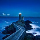 Tranquil night landscape with two lighthouses, moon, calm sea, boat, and vibrant