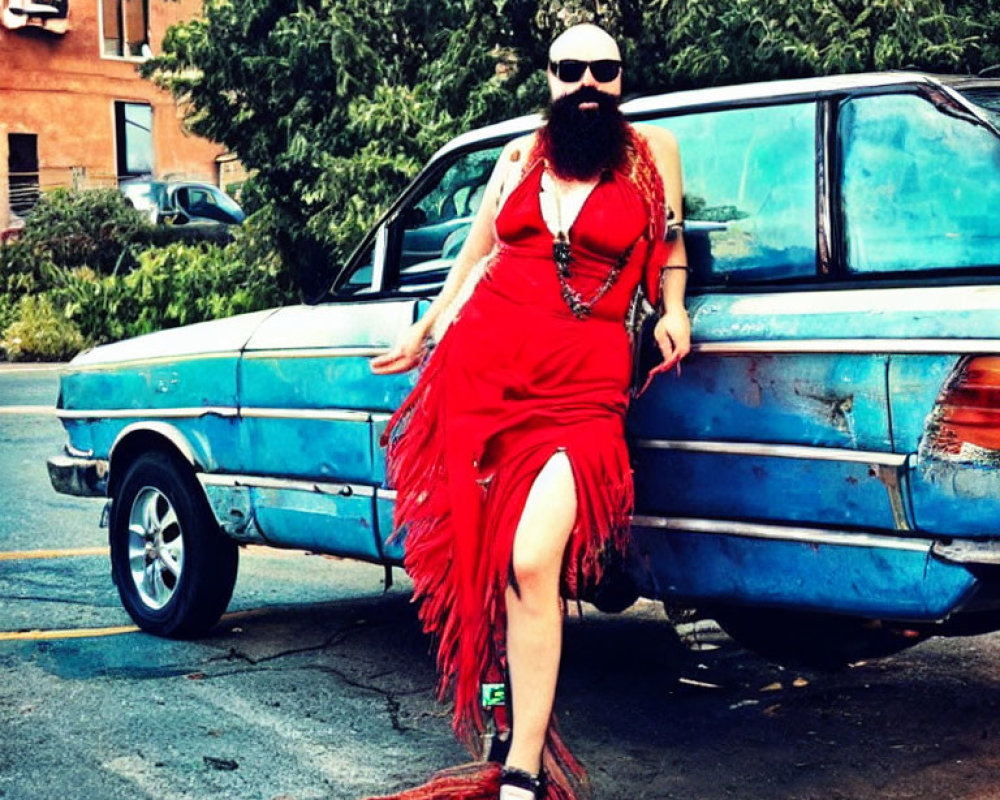 Bearded person in sunglasses leaning on blue car in red dress