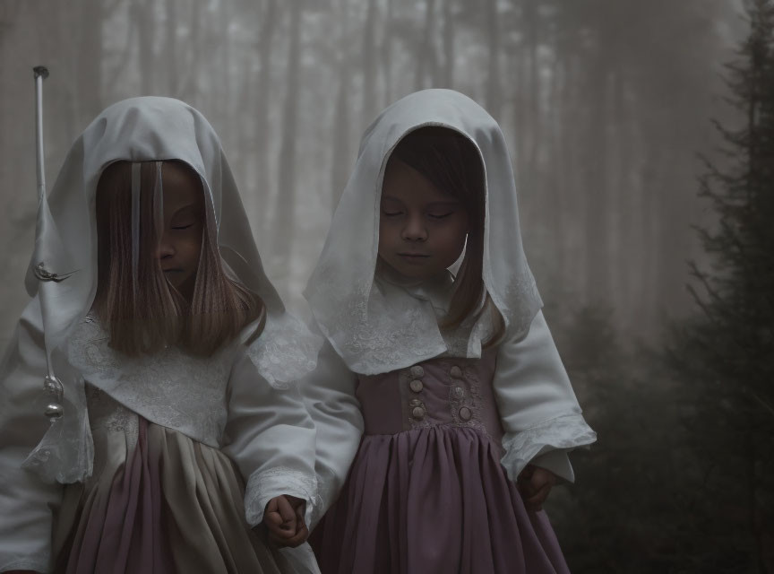 Children in vintage dresses walk through misty forest in white hoods