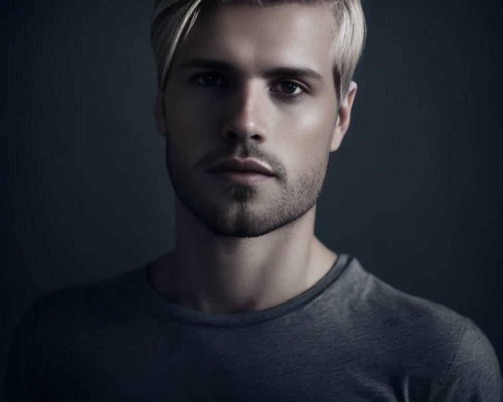 Blond man with short beard in gray T-shirt on dark background