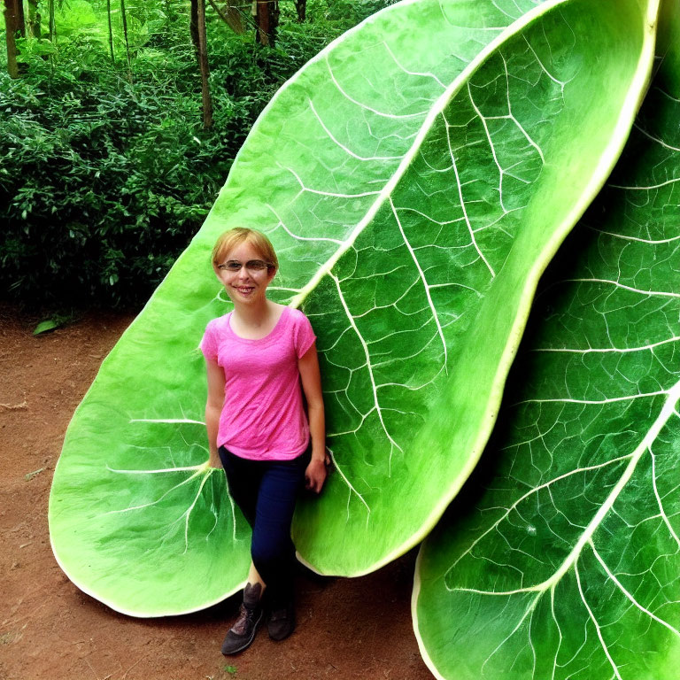 Smiling person with glasses next to oversized leaf in green environment