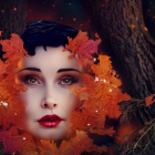 Woman's face framed by red and orange autumn leaves and partially covered by a single leaf