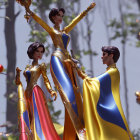 Three dolls in elegant blue and gold gowns with capes, one holding a goblet aloft