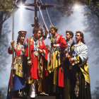 Five individuals in ornate ceremonial attire standing in front of a large cross