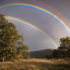 Double rainbow over serene landscape with tall trees and rolling hills