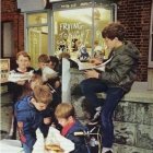Group of boys in uniforms eating fish and chips outside quaint shop