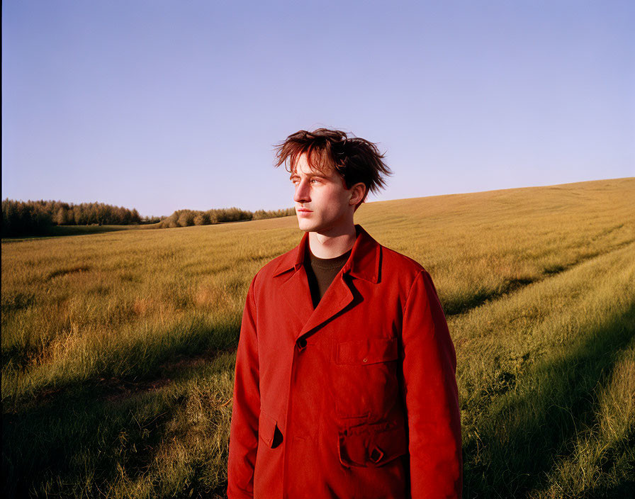 Tousled hair person in red jacket in lush field landscape