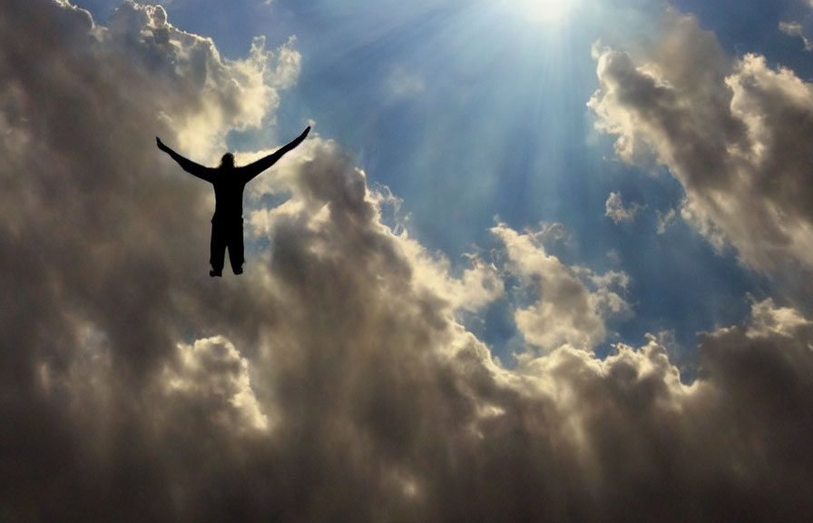 Person's silhouette with raised arms under dramatic sky with sunbeams.