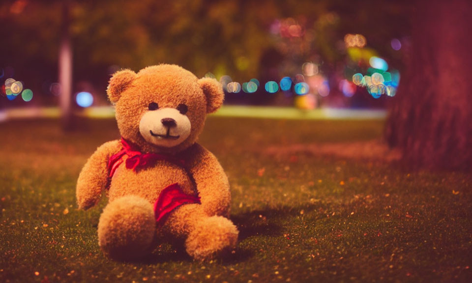 Red Bow Teddy Bear Sitting on Grass with Colorful Lights Background