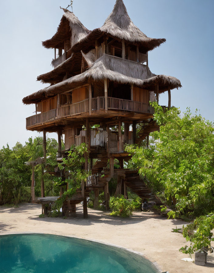 Wooden treehouse with thatched roofs by blue pool in lush greenery
