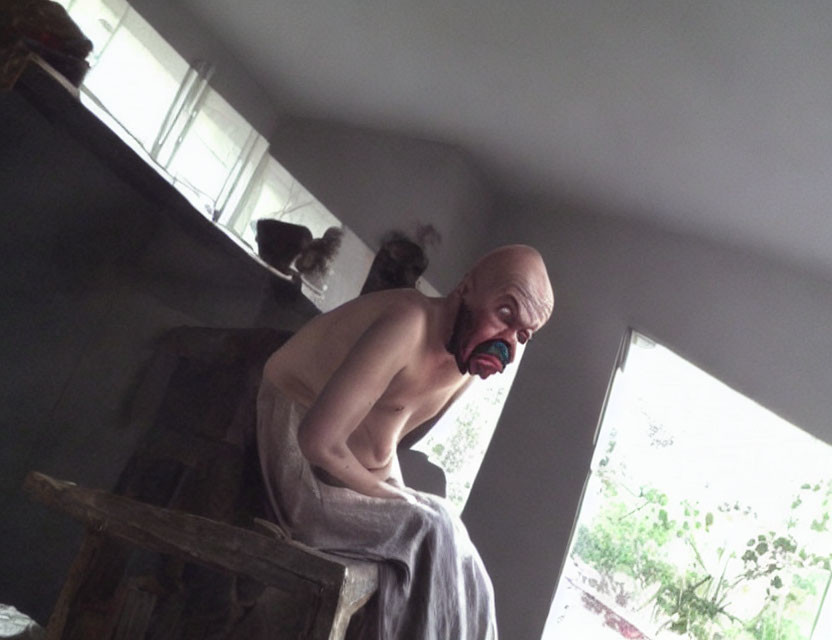 Person in Bald Cap and Scary Mask on Stool in Dimly Lit Room