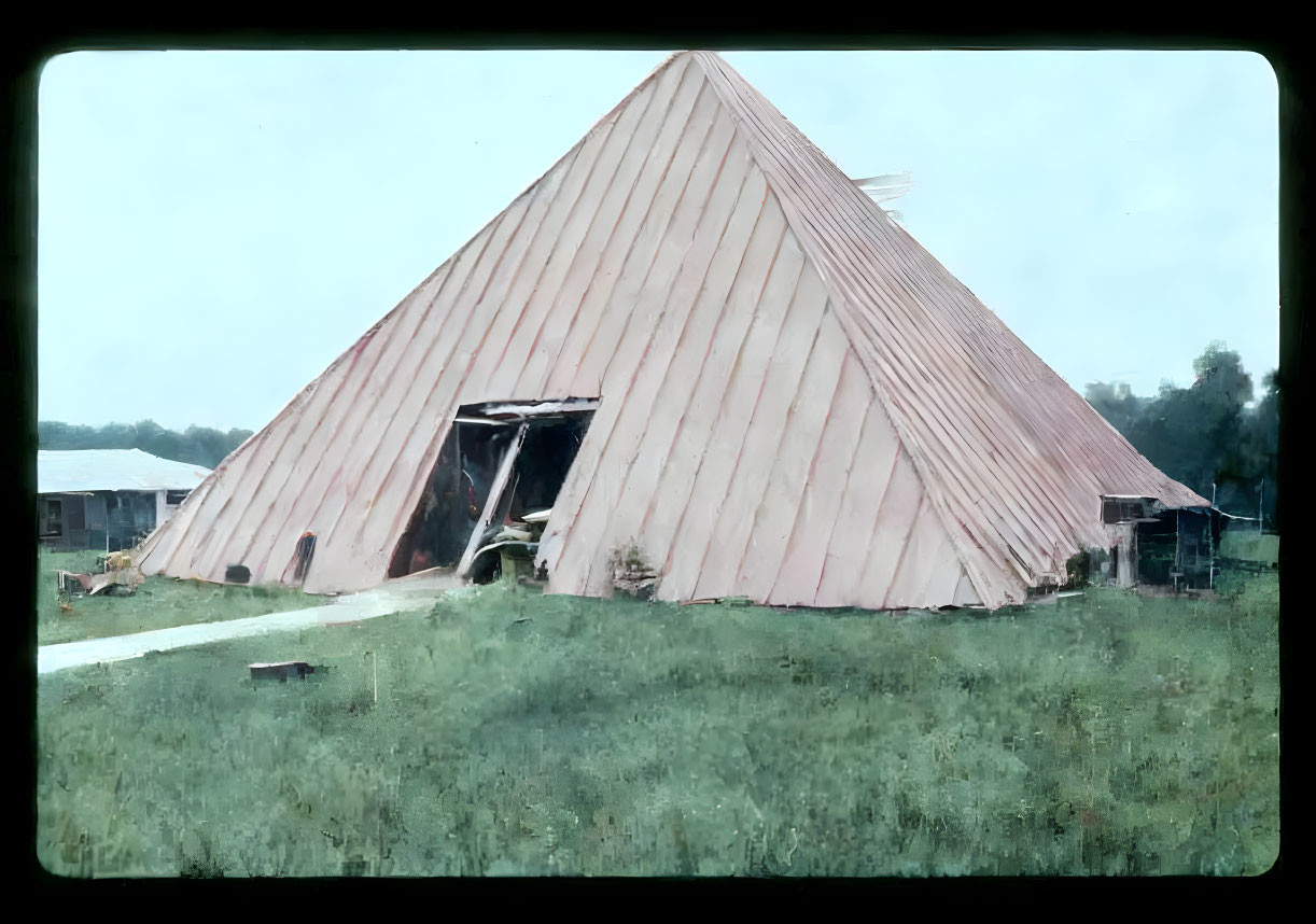 Vintage photograph of large triangular wooden barn with sloped roof and overgrown grass