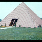 Vintage photograph of large triangular wooden barn with sloped roof and overgrown grass