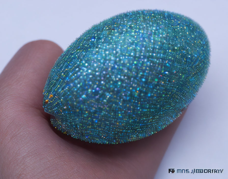 Shiny Turquoise and Blue Speckled Egg on Human Finger