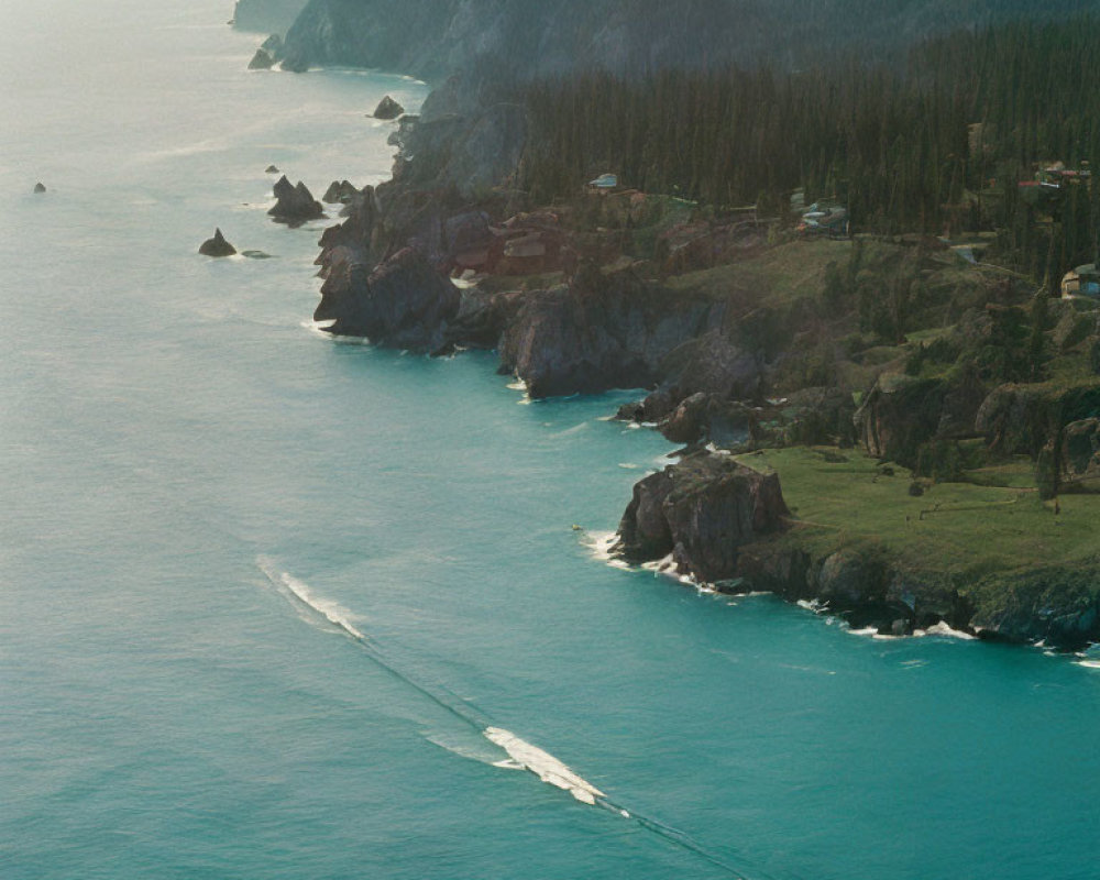 Rugged coastline with cliffs, pine trees, scattered buildings, and boat on turquoise sea