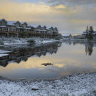 Snow-covered village by calm lake with wildlife at dusk